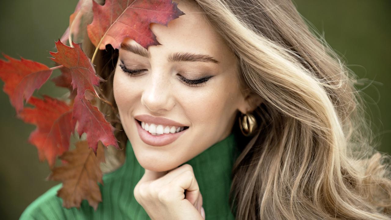 Beautiful girl outdoors in autumn fall. Young woman collects yellow fall leaves in autumn. Beauty woman holds autumn yellow leaf fall the face. Portrait of sensual woman over autumn fall background.