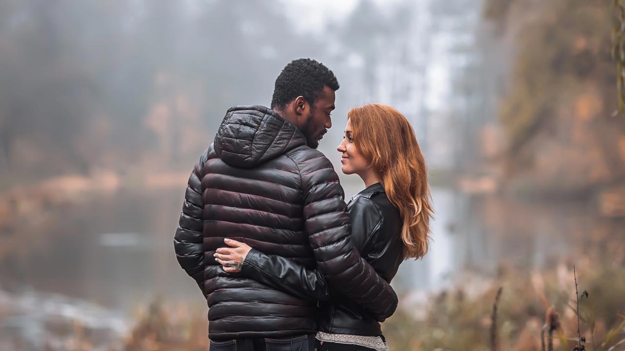 Interracial couple posing in autumn leaves background, black man and white redhead woman