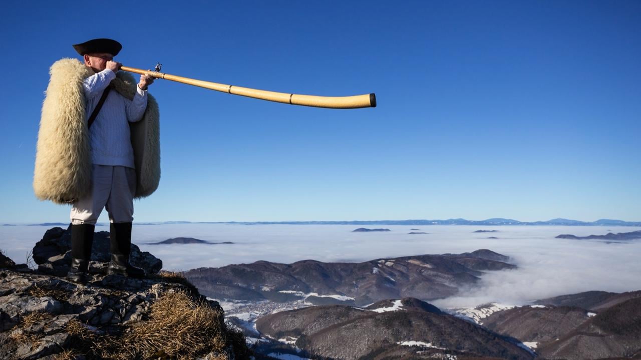 Na snímke muž v tradičnom pastierskom oblečení hrá na hudobný nástroj trombitu na vrchu Kľak (1 351,6 m n. m.) v nedeľu 19. januára 2025 v Lúčanskej Malej Fatre na hranici okresov Žilina a Martin. FOTO TASR - Daniel Stehlík