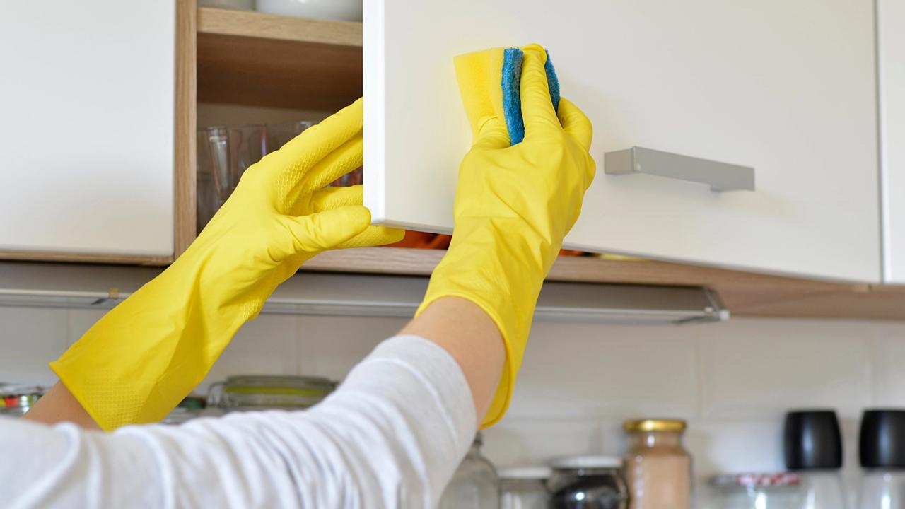 woman in yellow gloves washes the door in kitchen cabinet