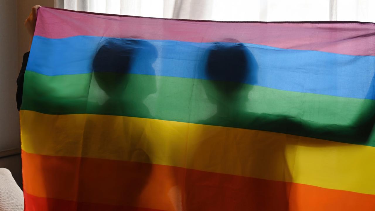 Behind view and silhouette of Pride young gay couple with hands raised and the LGBT flag, LGBT, pride, relationships and equality concept