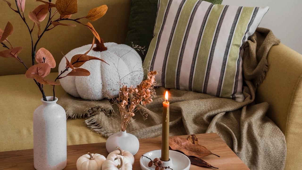 Autumn interior of the living room - sofa with pillows and blankets, wooden bench with autumn decor  