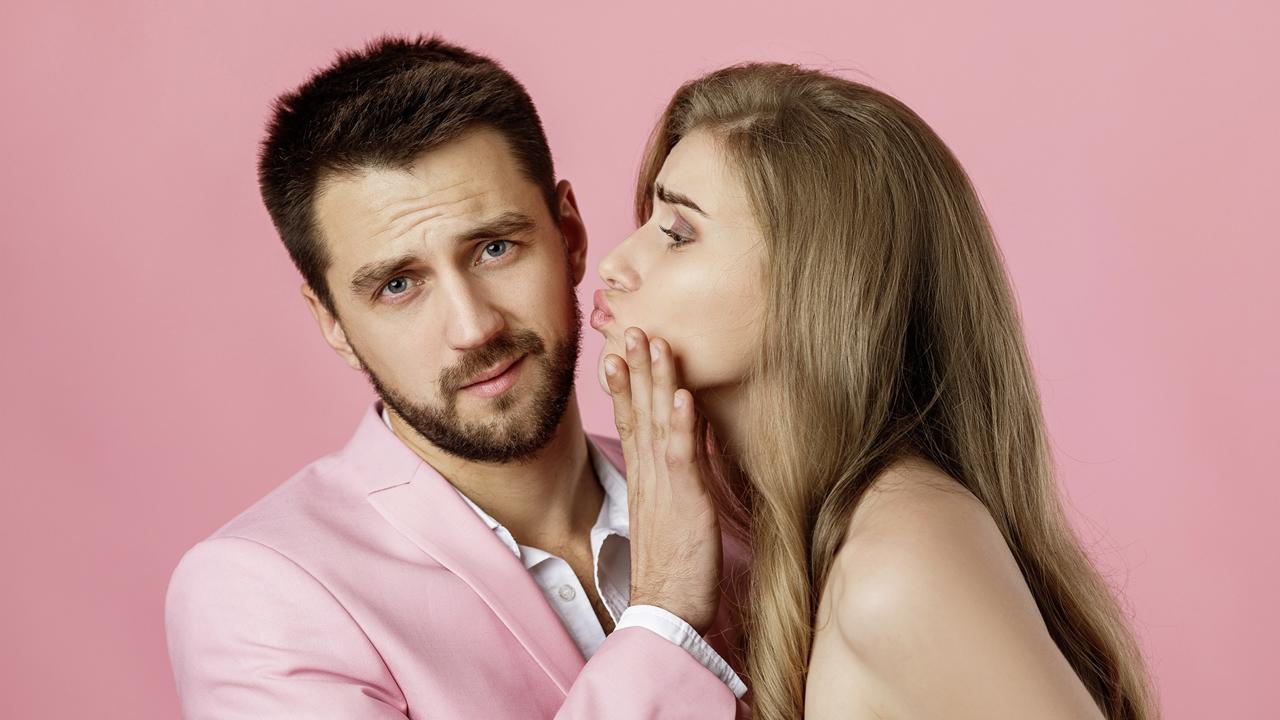 woman want to kiss her boyfriend and he does not want on pink background. man refuses kiss from girlfriend, shows stop gesture