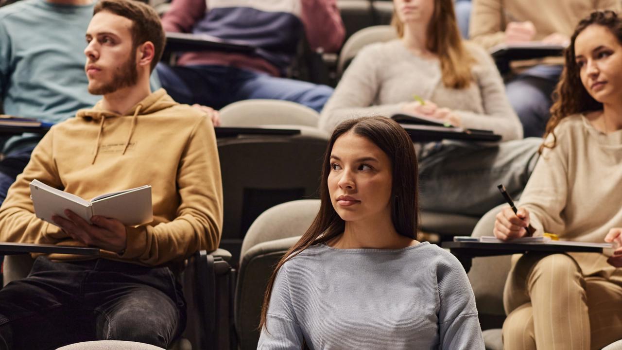 Large group of university students paying attention on a lecture at amphitheater. Focus is on woman in the foreground.