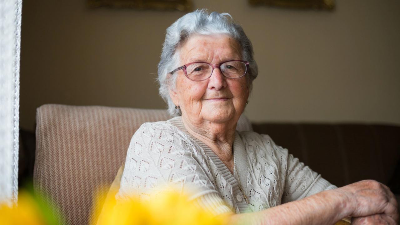 Portrait of a beautiful old woman with gray hair and glasses is sitting in a chair in her home.