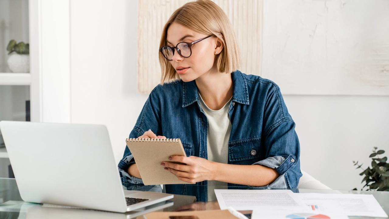 Young,Woman,Taking,Notes,Using,Laptop,For,Remote,Studies,At