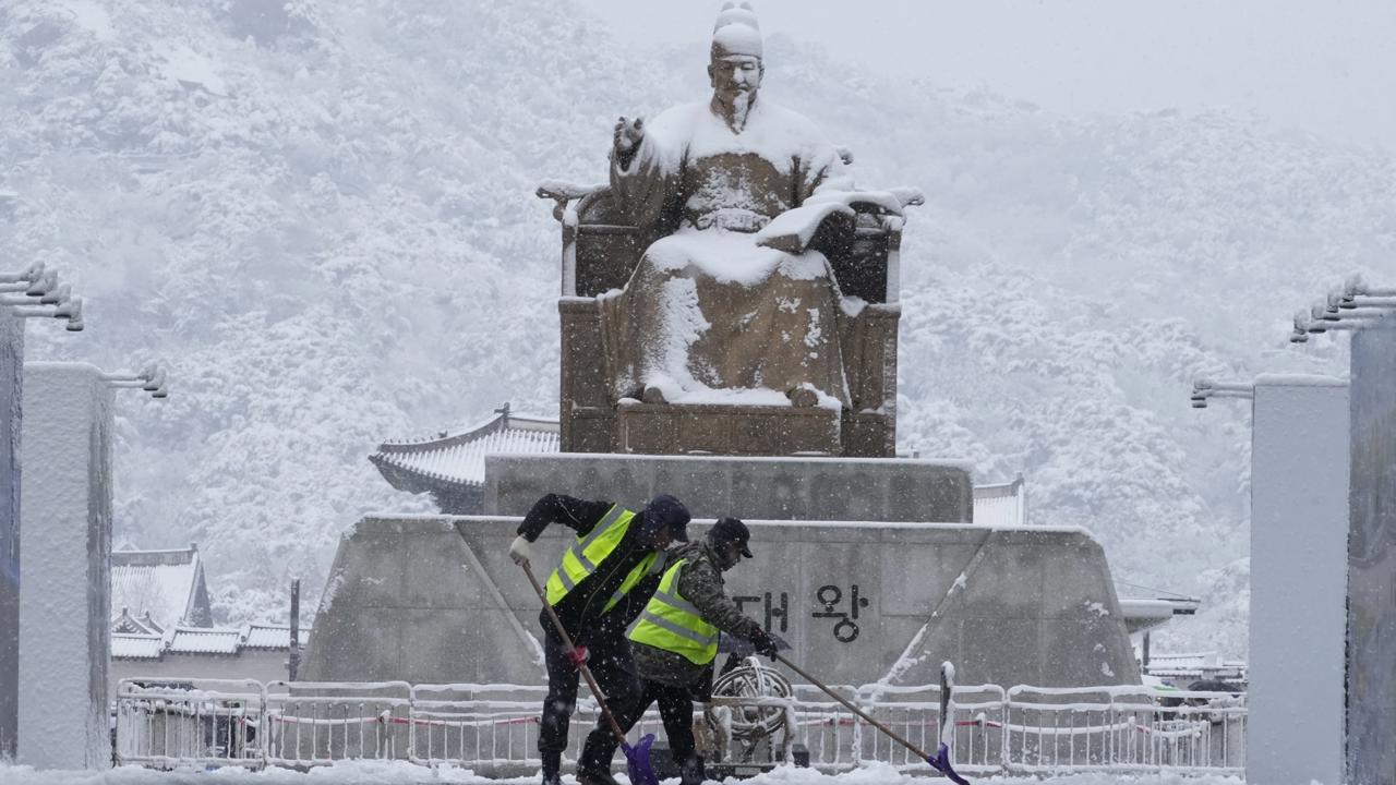 Na snímke zamestnanci mesta odhrabávajú sneh pred bronzovou sochou  kórejského kráľa Sedžonga, ktorý zaviedol kórejské písmo (hangul), na Námestí Kwanghwamun v juhokórejskej metropole Soul v stredu 27. novembra 2024.  FOTO TASR/AP