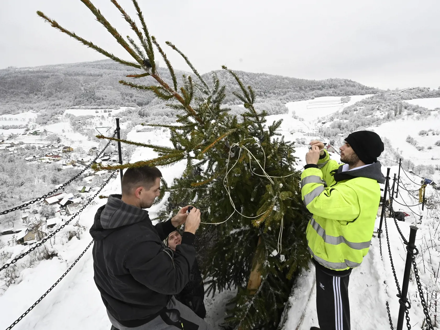 Na snímke skupina chlapov pripevňuje osvetlenie vianočného stromčeka na brale hradu Lednica 11. decembra 2021. Hradné bralo nad obcou Lednica (okres Púchov) aj tento rok už tradične zdobí živý vianočný stromček s farebným osvetlením, ktorý sem vyniesla a vyzdobila skupina chlapov z obce. FOTO TASR - Radovan Stoklasa