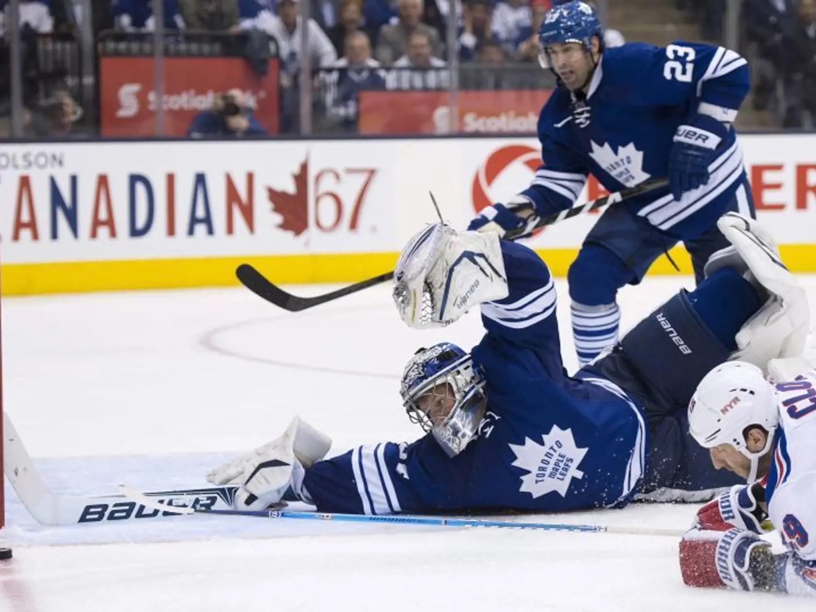 Brankár Toronta James Reimer sa snaži zastaviť strelu Ryana Clowa z NY Rangers, prizerá sa Ryan O'Byrne.
