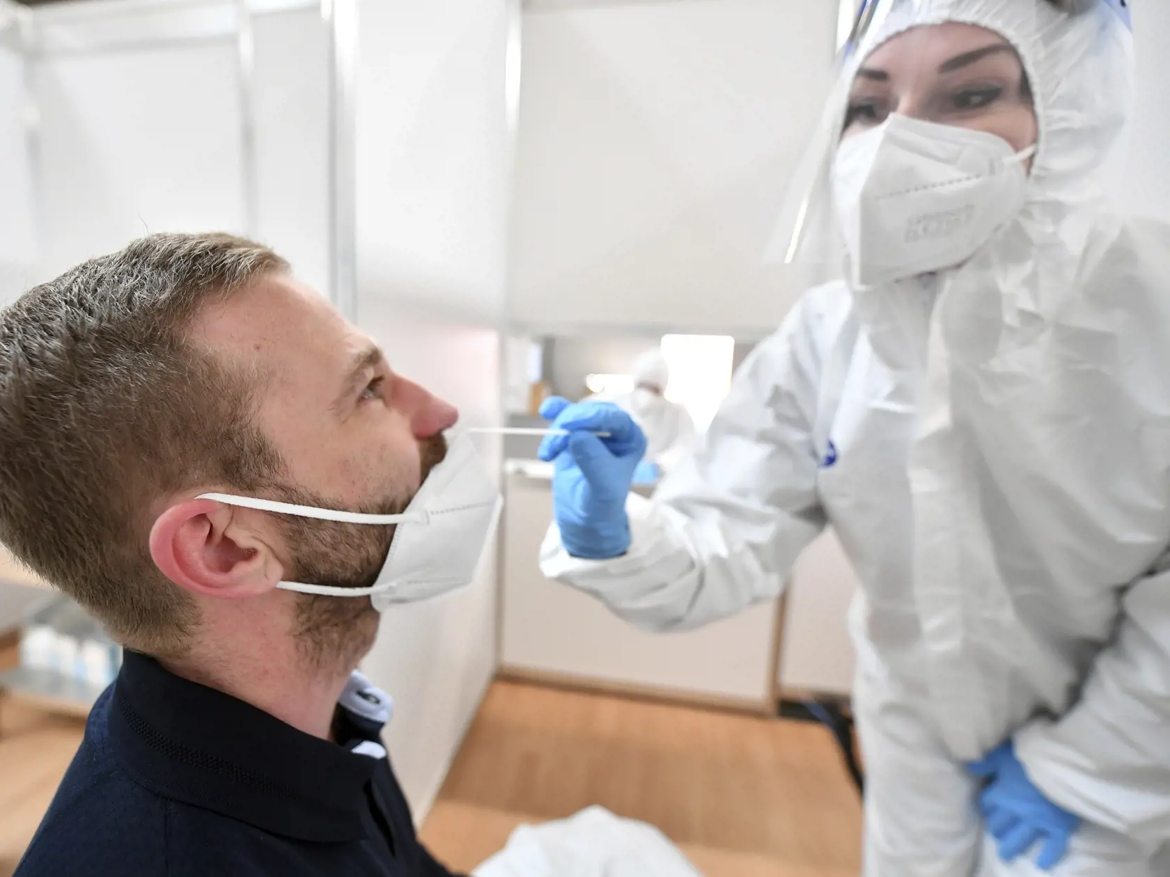 Zdravotníčka v ochrannom odeve odoberá vzorku mužovi počas testovania na ochorenie COVID-19.