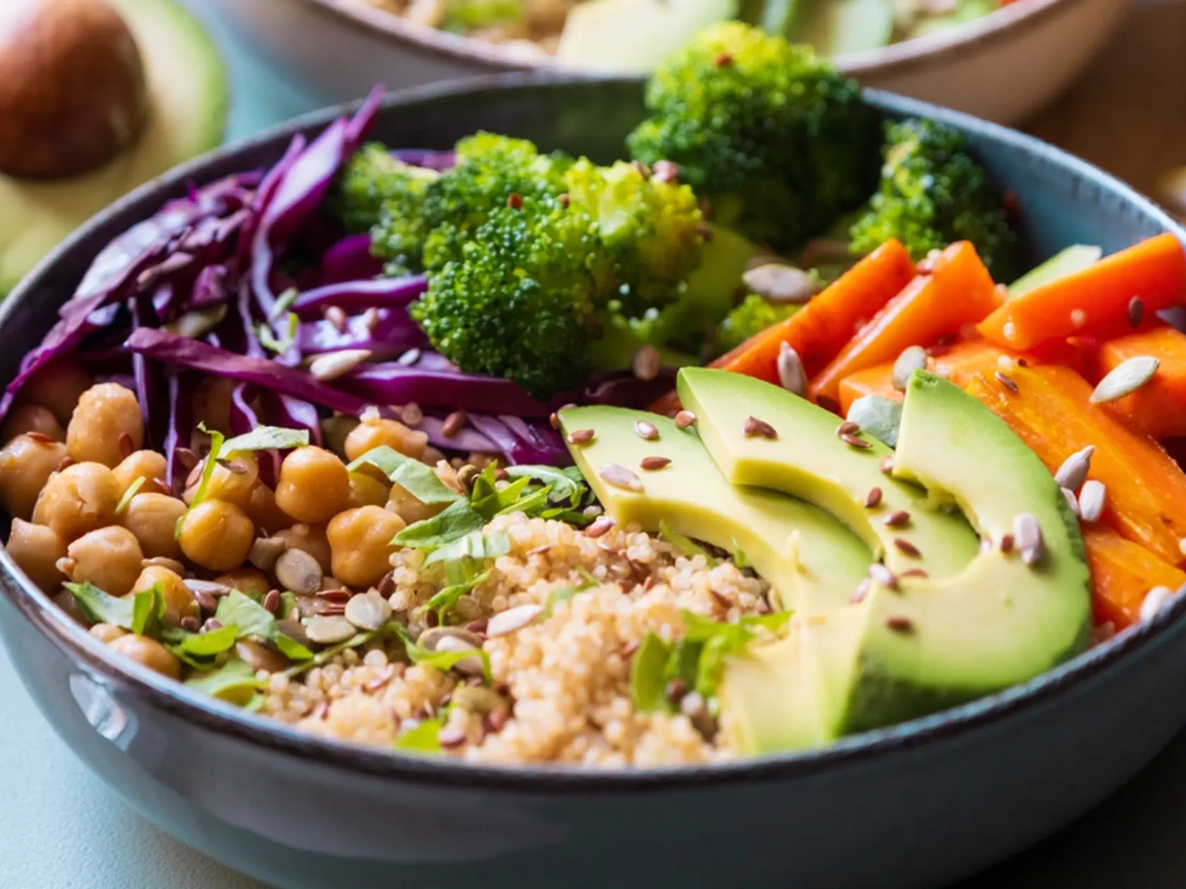 A vibrant vegan quinoa bowl with creamy avocado, protein-packed chickpeas, fresh broccoli, sweet carrots, and crisp red cabbage. A wholesome, plant-based meal full of color and nutrition.