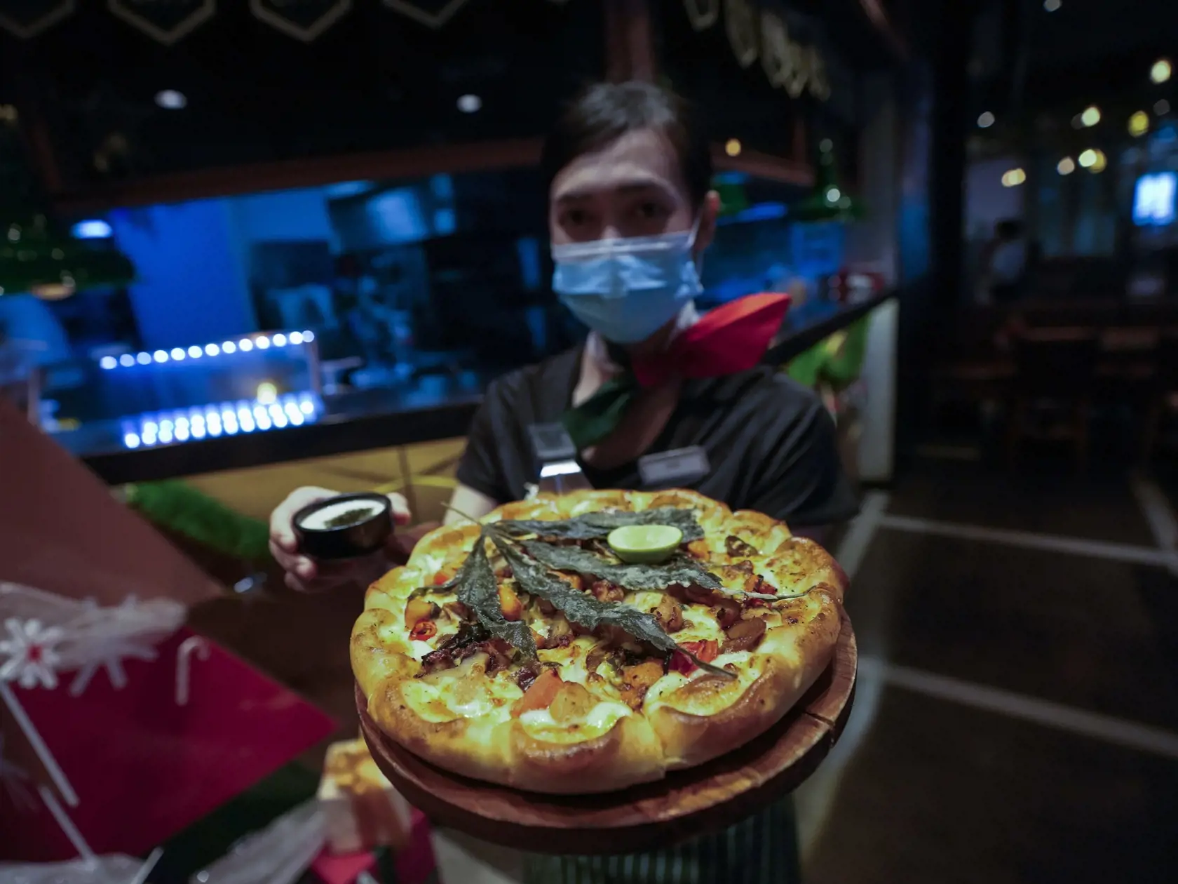 Zamestnankyňa ukazuje pizzu s listom marihuany v reštaurácii v Bangkoku 24. novembra 2021. The Pizza Company, hlavný thajský reťazec rýchleho občerstvenia, tento mesiac propaguje svoj produkt "Crazy Happy Pizza“ s listom marihuany. FOTO TASR/AP