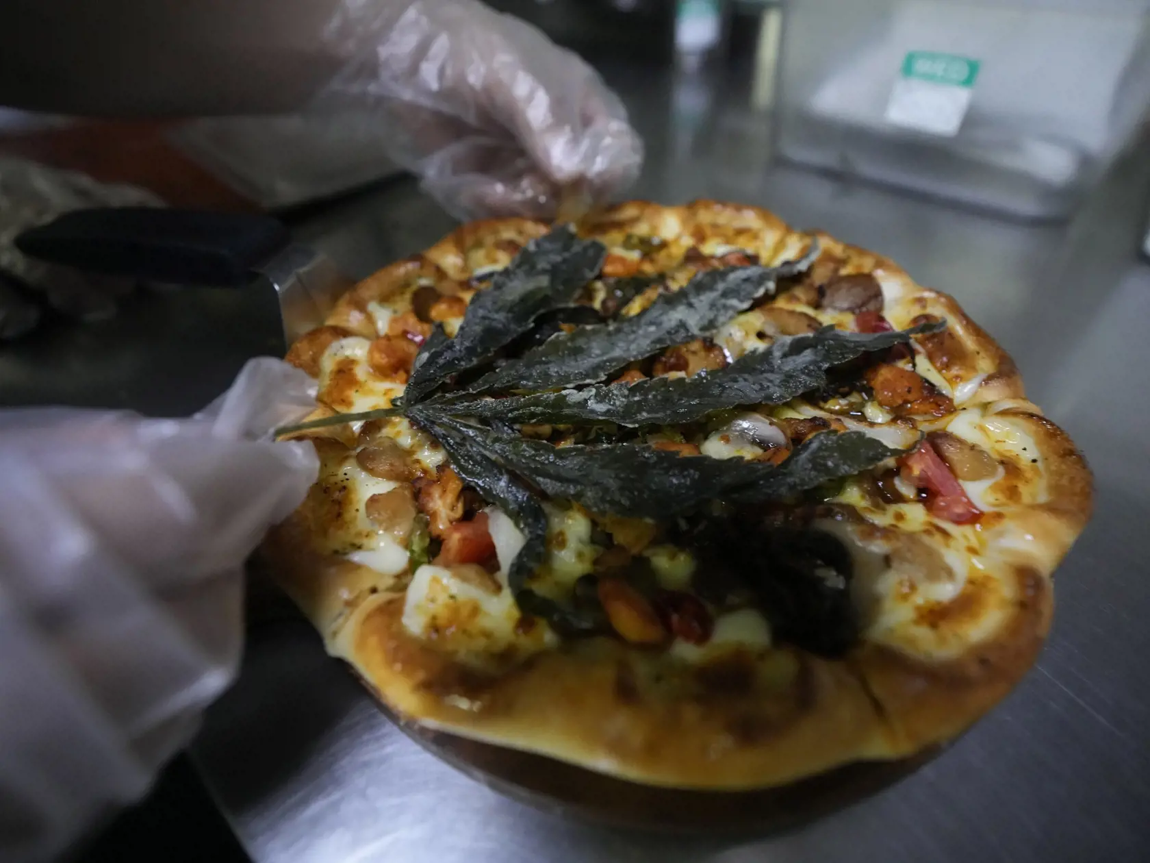 Zamestnanec pripravuje pizzu s listom marihuany v reštaurácii v Bangkoku 24. novembra 2021. The Pizza Company, hlavný thajský reťazec rýchleho občerstvenia, tento mesiac propaguje svoj produkt "Crazy Happy Pizza“ s listom marihuany. FOTO TASR/AP