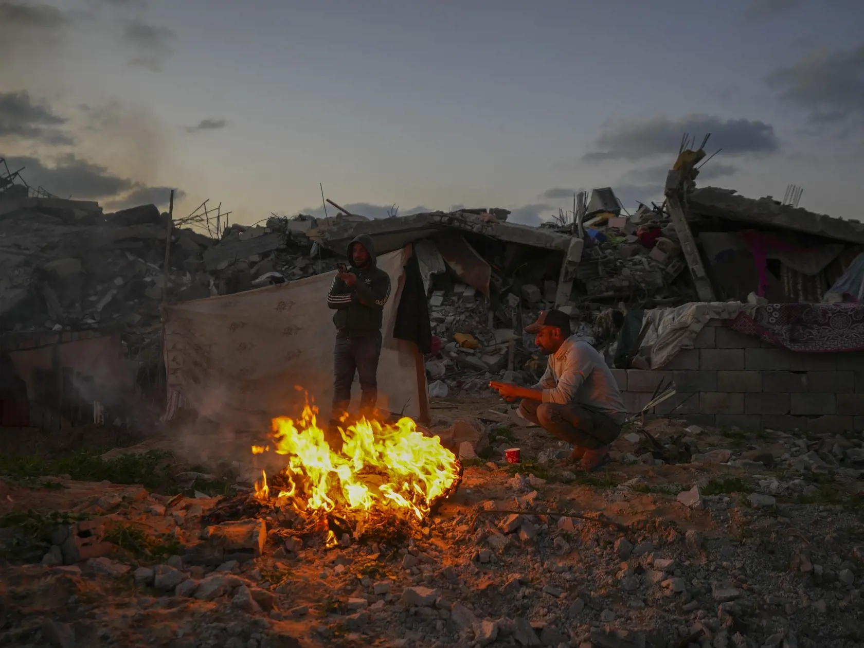 Na snímke muž sedí pri ohni medzi troskami a zničenými budovami počas bojov medzi izraelskom armádou a palestínskym militantným hnutím Hamas v meste Gaza v utorok 4. februára 2025.