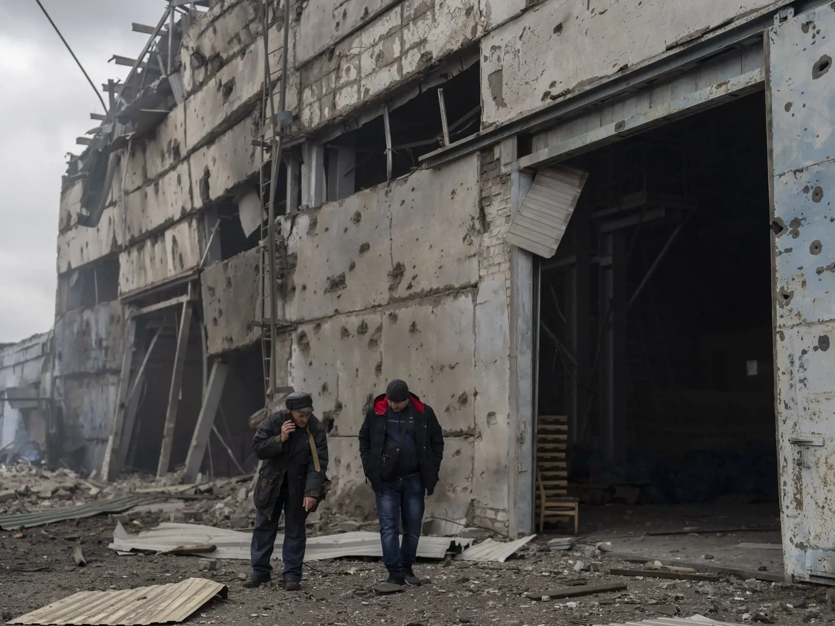 Dvaja muži stoja pred zničeným závodom po ruskom ostreľovaní vo východoukrajinskom meste Kramatorsk počas 50. dňa ruskej invázie na Ukrajinu vo štvrtok 14. apríla 2022.
