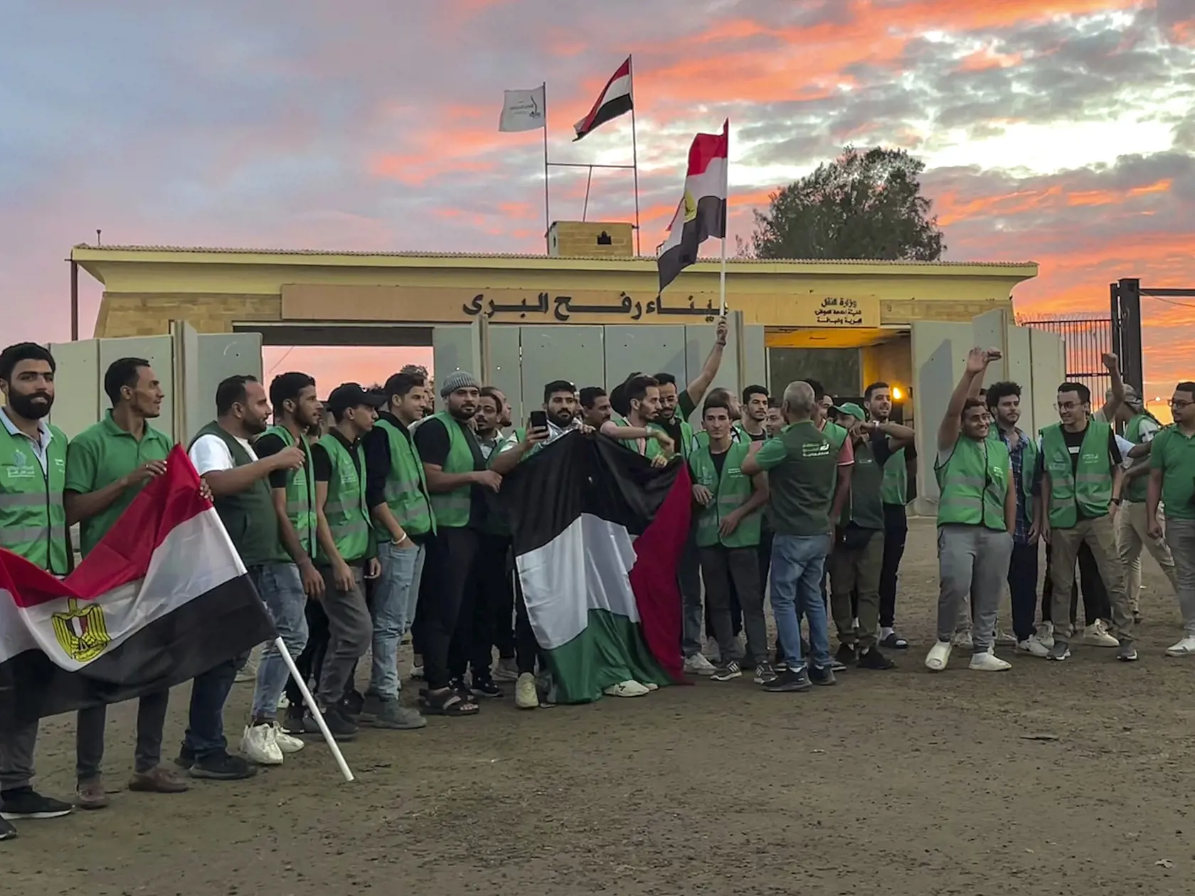 JB 15 Rafah - Dobrovoľníci konvoja s humanitárnou pomocou pre pásmo Gazy mávajú egyptskými a palestínskymi zástavami na hraničnom priechode Rafah medzi Egyptom a Gazou 17. októbra 2023. Konvoje s humanitárnou pomocou sa v utorok pohli z egyptského vnútrozemia smerom k hraničnému priechodu Rafah spájajúcemu Egypt a pásmo Gazy, informuje TASR podľa správy agentúry AFP. Predstaviteľ Červeného kríža váhavo potvrdil, že rokovania o vstupe konvojov do pásma Gazy a odchode cudzincov sa blížia k záveru.