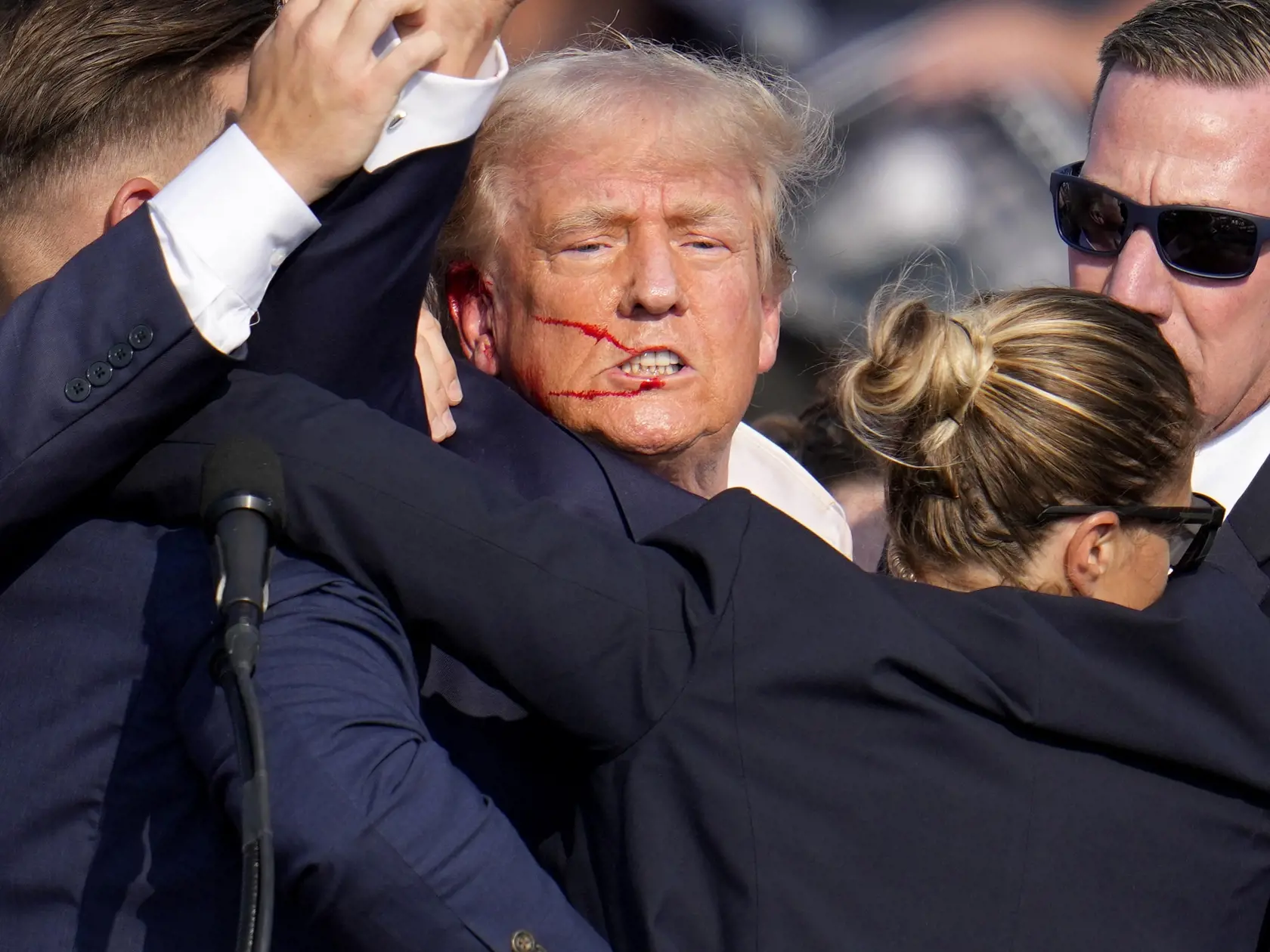 Republikánsky prezidentský kandidát Donald Trump (uprostred) reaguje pri odchode za pomoci ochrankárov z predvolebného mítingu v meste Butler v americkom štáte Pensylvánia 13. júla 2024. Trump potvrdil, že v sobotu na mítingu v Pensylvánii ho zasiahla guľka. Tá mu prestrelila hornú časť pravého ucha. Bývalý americký prezident sa vyjadril na sociálnej sieti, informuje TASR.