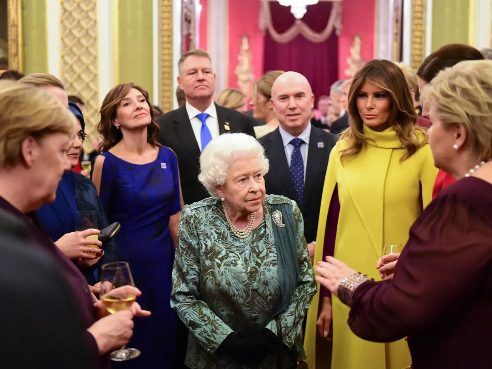 Summit NATO: Kráľovná Alžbeta, po jej boku Melania Trump v žltom kabáte a bývalá nemecká kancelárka Angela Merkelová.