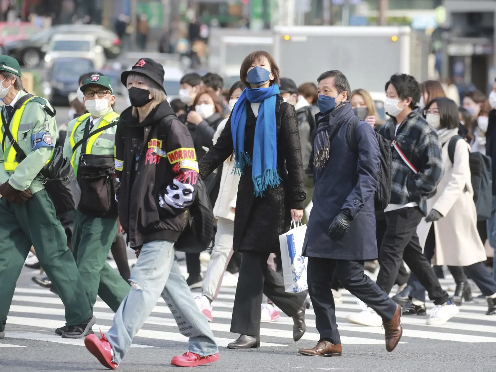 Ľudia s ochrannými rúškami na tvári kráčajú cez cestu v Tokiu v stredu 19. januára 2022. Japonská vláda schválila v stredu nové obmedzenia proti koronavírusu pre veľkú časť krajiny vrátane hlavného mesta Tokio. Snaží sa tak bojovať proti rekordnému počtu prípadov nákazy, pripisovanému variantu omikron. Obmedzenia v 13 regiónoch, ktoré sú zacielené na nočný život a sú oveľa menej prísne než celoplošný lockdown, budú platiť od piatka 21. januára do polovice februára.