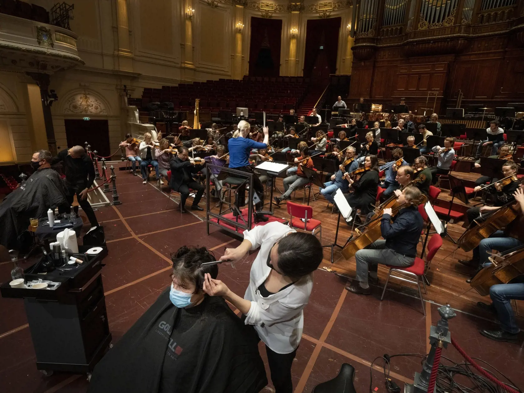 Kaderníci strihajú zákazníkov na pódiu počas skúšky Kráľovského orchestra Concertgebouw v Amsterdame v stredu 19. januára 2022. Múzea, divadlá a koncertné sály v stredu pozvali do svojich priestorov kaderníkov, pedikérky a majiteľov ďalších prevádzok, ktoré holandská vláda povolila otvoriť na protest proti pokračujúcemu zatvoreniu kultúrnych inštitúcií.