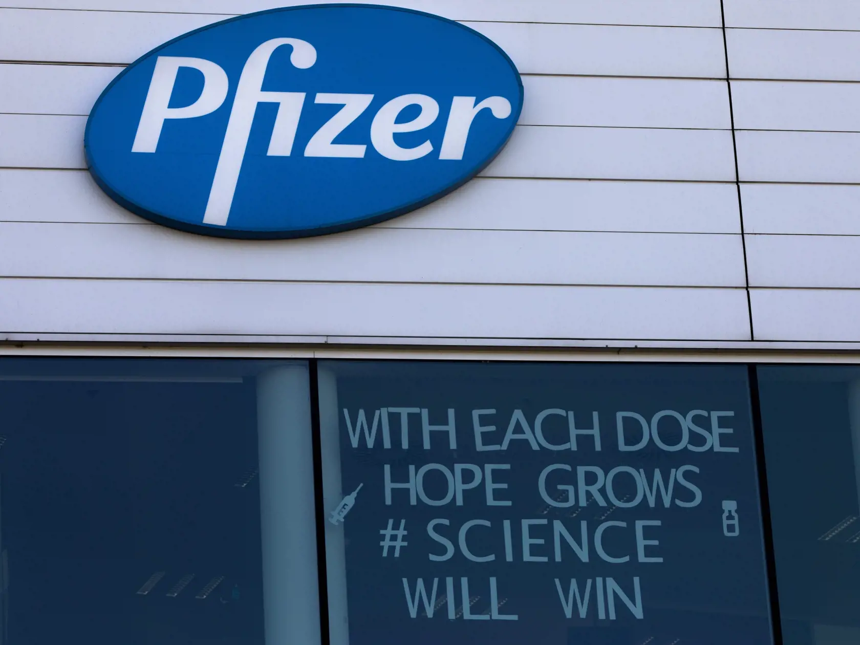KK17 Puurs - Na snímke logo Pfizeru vo výrobnom centre spoločnosti v belgickom meste Puurs v utorok 23. februára 2021. Očkovanie proti novému koronavírusu výrazne prispieva k zníženiu počtu hospitalizovaných pacientov. Vyplýva to z výsledkov dvoch britských štúdií, ktoré boli zverejnené v pondelok.  Prvá štúdia bola vykonaná v Škótsku a podieľali sa na nej vedci z univerzít v Edinburghu a Glasgowe a tiež odborníci z regionálneho úradu verejného zdravotníctva. FOTO TASR/AP
A sign is pasted into a