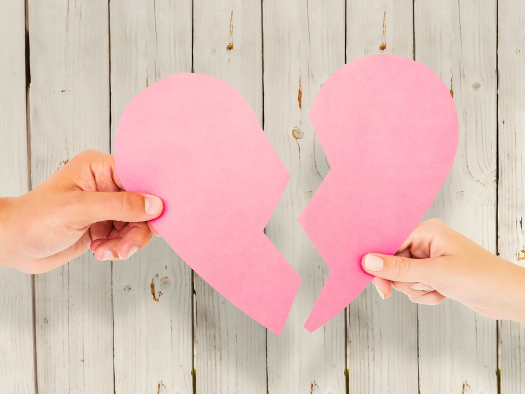 Couple,Holding,Two,Halves,Of,Broken,Heart,Against,Wooden,Background