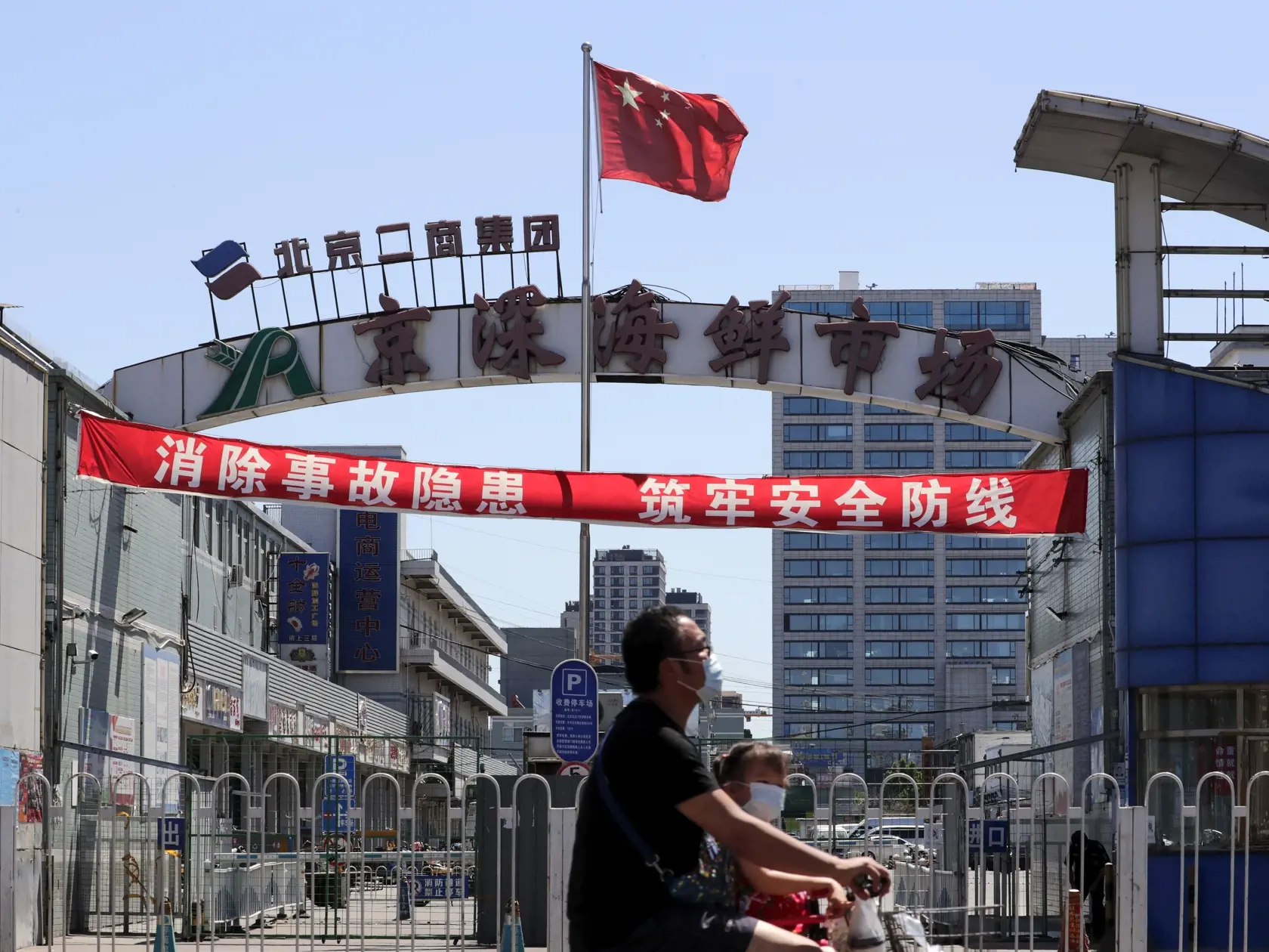 JB 40 Peking - Muž a dieťa s ochrannými rúškami na tvári na zabránenie šíreniu nového koronavírusu prechádzajú na elektrickej kolobežke okolo veľkoobchodného trhu s rybami a inými morskými živočíchmi, ktorý je zavretý pre inšpekciu v čínskom Pekingu 14. júna 2020. Čína oznámila v nedeľu 57 nových prípadov nákazy koronavírusom, čo je najviac za jeden deň od apríla. Údaje prišli v čase, keď rastú obavy z opätovného rozšírenia koronavírusovej choroby. Nové ohnisko nákazy však bolo teraz spojené s t