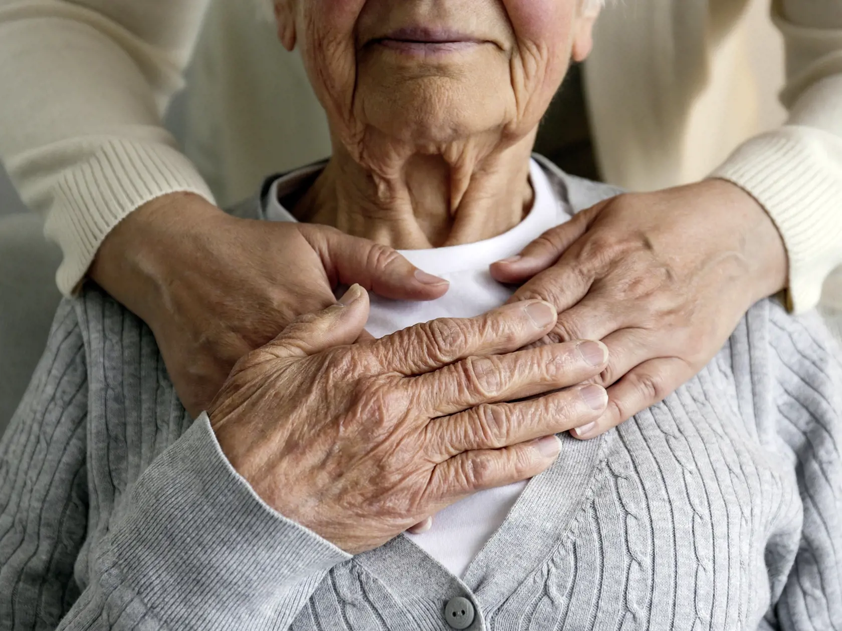 Unrecognizable female expressing care towards an elderly lady, hugging her from behind holding hands. Two adult women of different age. Family values concept. lose up, copy space, background.