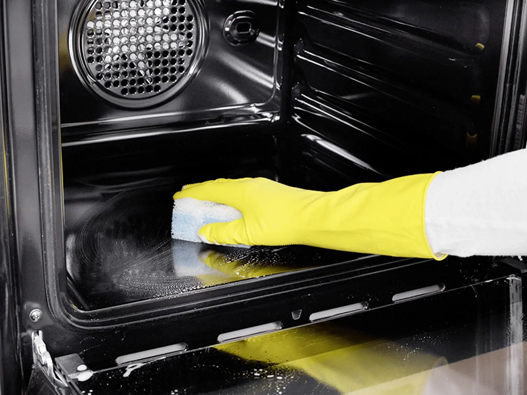 Close up of female hand with yellow protective gloves cleaning oven