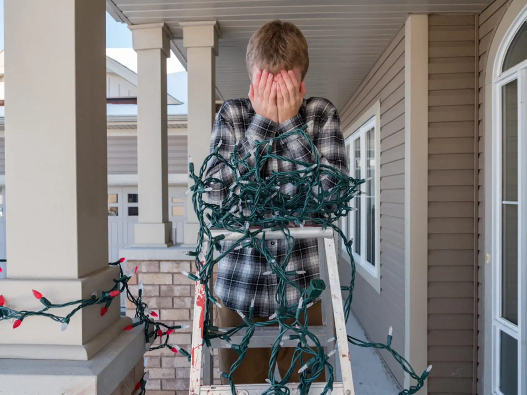 Man,Frustrated,On,A,Ladder,While,Hanging,Tangled,Holiday,Lights.
