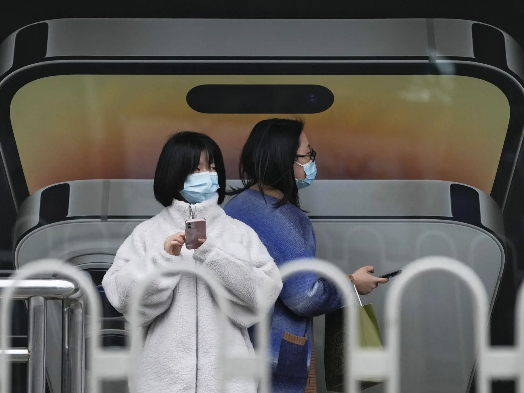 KK16 Peking - Žena s ochranným rúškom na tvári prechádza okolo inej ženy, ktorá používa iPhone počas čakania na autobus na autobusovom zastávke v Pekingu 30. októbra 2022. Čínske úrady vyhlásili v stredu 2. novembra 2022 lockdown v oblasti okolo najväčšej továrne na výrobu iPhonov na svete po zistení koronavírusu a úteku tamojších zamestnancov. FOTO TASR/AP
A woman wearing a face mask walks by another using an iPhone as they waiting for their buses at a bus stand displaying an iPhone advertiseme
