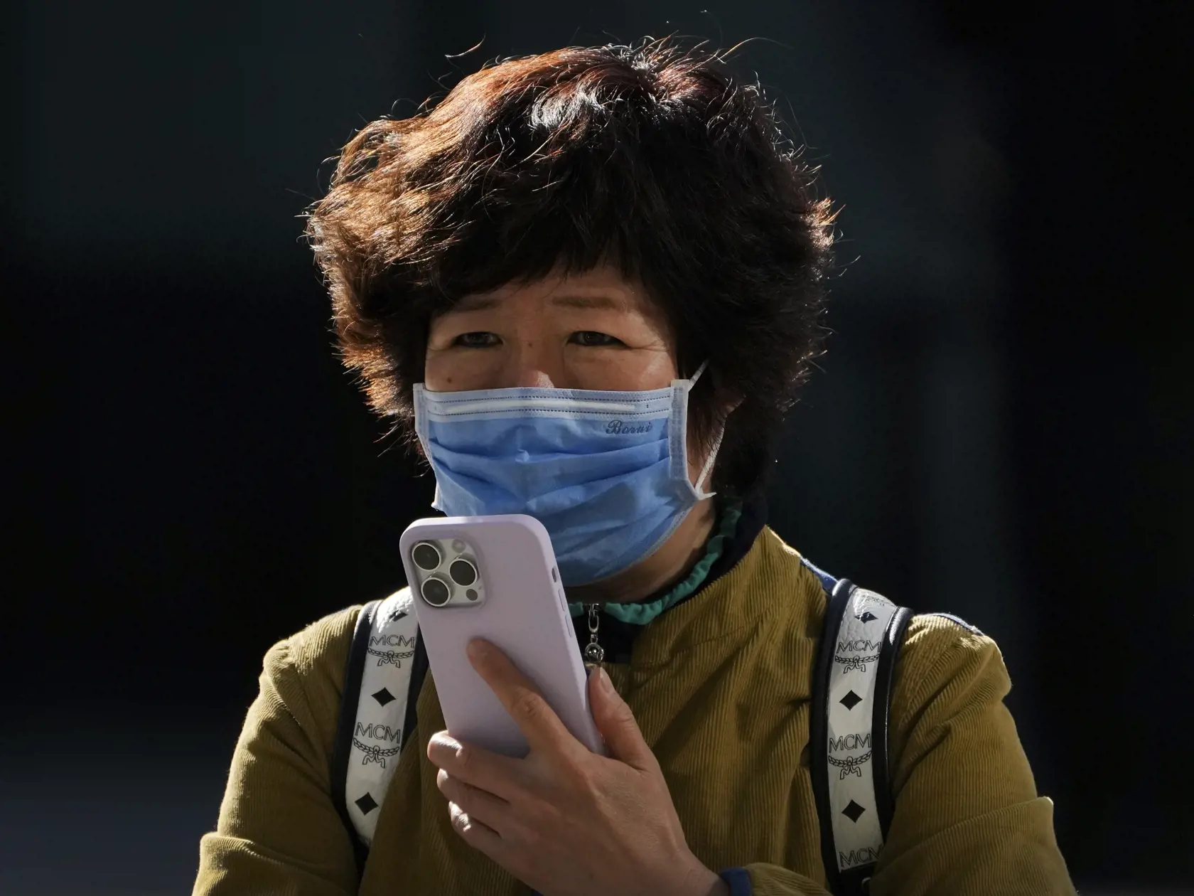 KK14 Peking - Žena s ochranným rúškom používa iPhone 7. novembra 2022 v Pekingu. Čína v pondelok hlásila najvyšší počet nakazených za posledných šesť mesiacov. Stalo sa tak napriek tomu, že komunistická vláda v Pekingu nepoľavuje v uplatňovaní čoraz nepopulárnejšej stratégie nulovej tolerancie covidu, spojenej so zavádzaním striktných lockdownov.  Americká spoločnosť Apple v nedeľu večer oznámila, že jej továreň v Čeng-čou funguje len vo výrazne obmedzenom režime. Upozornila preto svojich zákazn