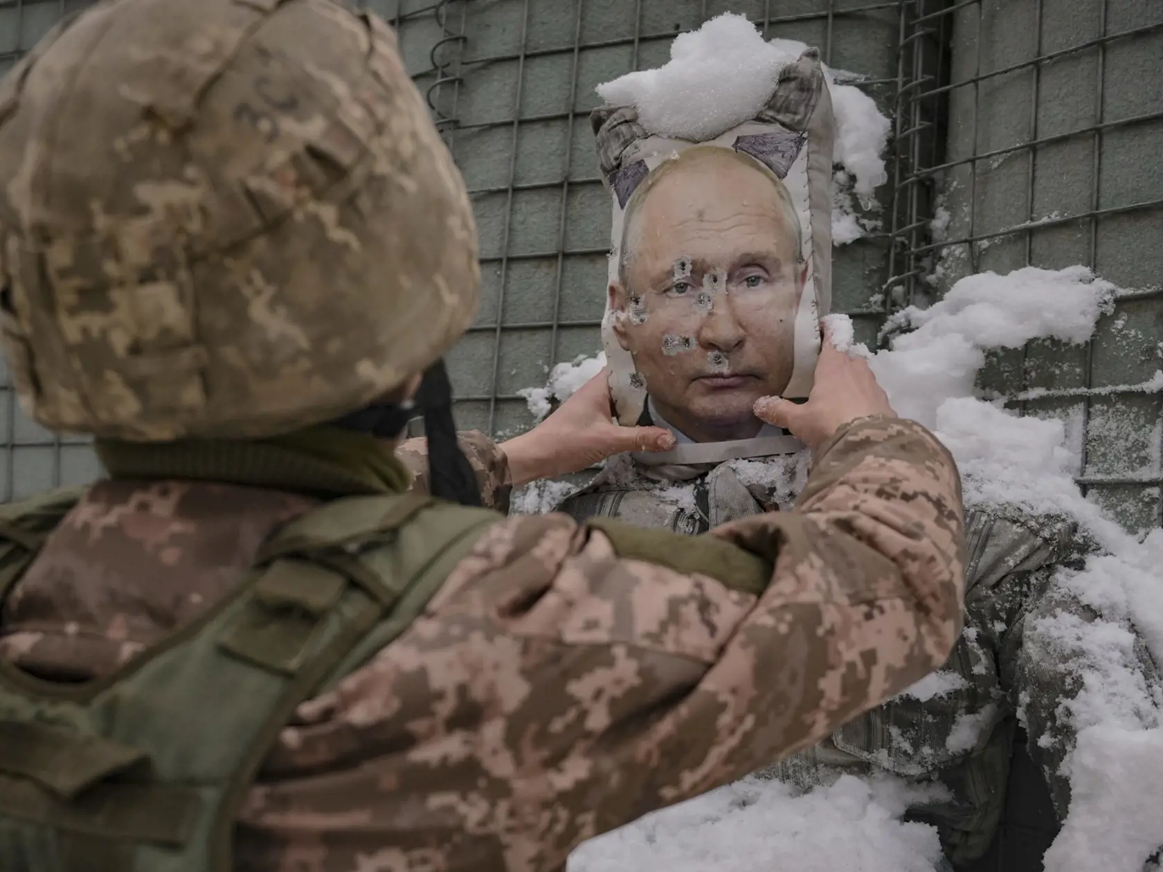 Ukrajinský vojak odstraňuje sneh z rozstrieľanej fotografie ruského prezidenta Vladimira Putina, ktorá sa nachádza na figuríne počas rozhovoru na frontovej línii v Luhanskej oblasti na východe Ukrajiny v utorok 1. februára 2022.