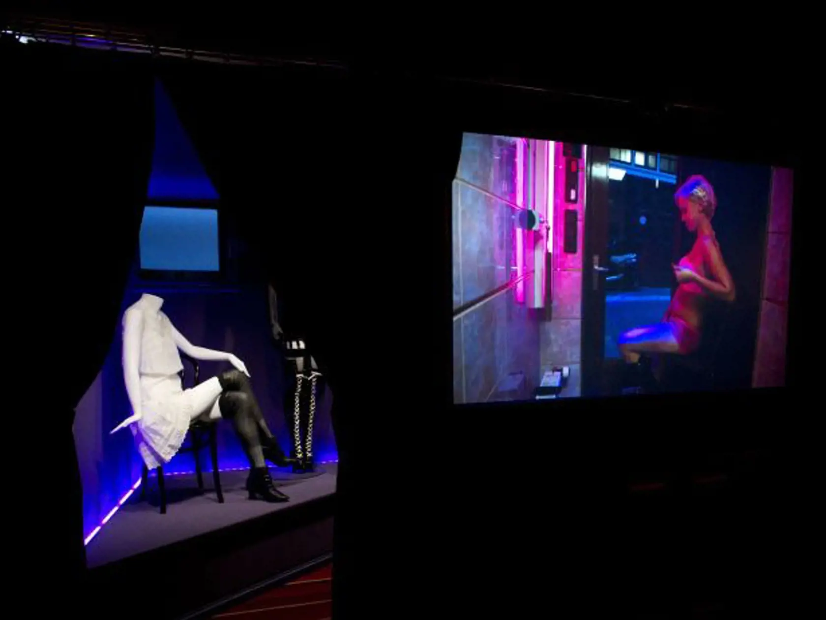 In this photo taken Tuesday, Feb. 4, 2014, a film showing prostitutes in their daily lives, right, and clothes prostitutes wore earlier in the 20th century, left, are shown at the 'Red Light Secrets' museum in Amsterdam. On any given evening, thousands of tourists stroll down the narrow streets of Amsterdam's famed Red Light District, gawking at ladies in lingerie who work behind windows, making a living selling sex for money. Now a small educational museum is opening in heart of the district th