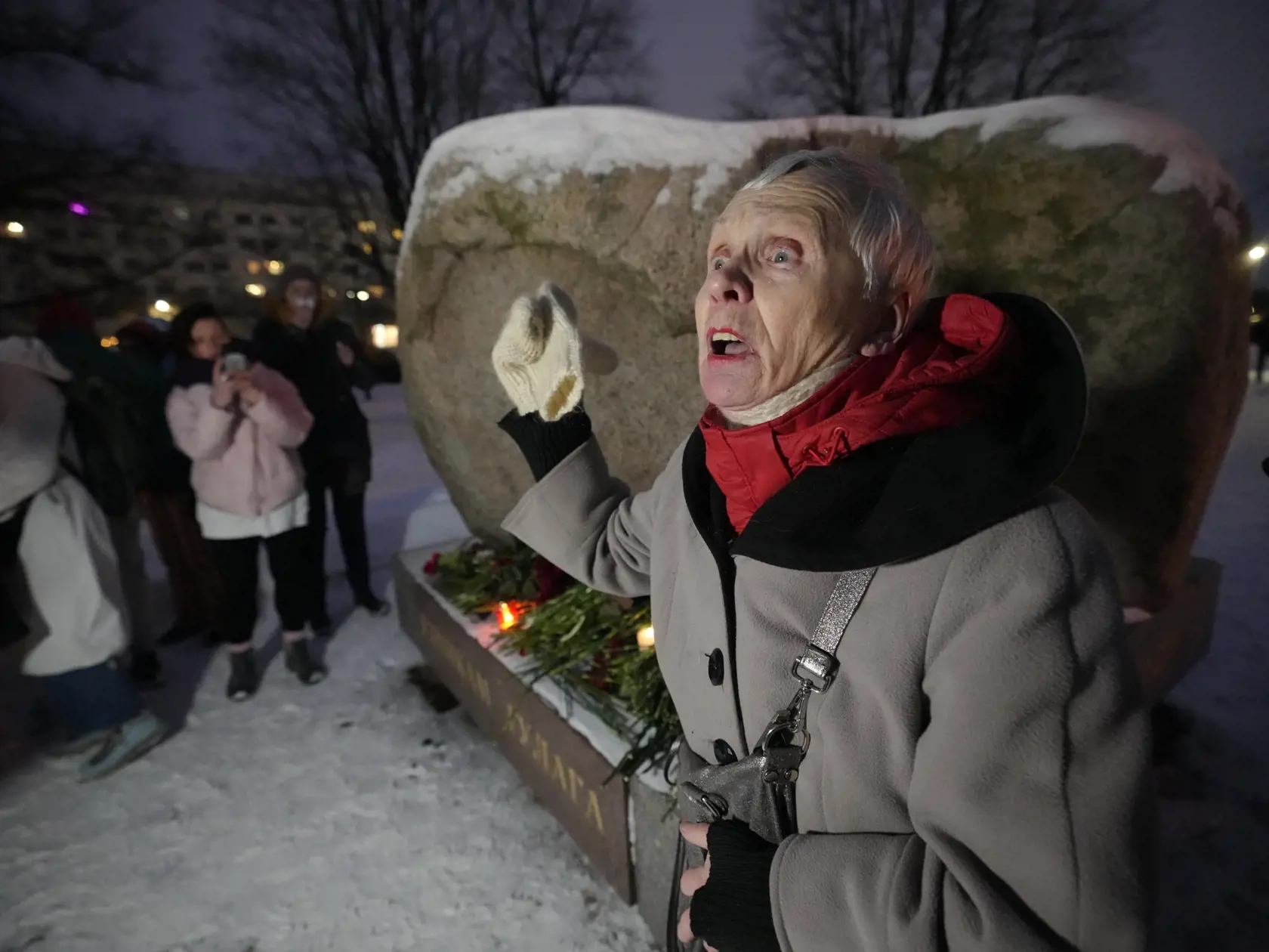 Osemdesiattriročná žena sa prihovára ľuďom, ktorí kladú kvety k pamätníku, veľkému balvanovi zo Sloveckých ostrovov v Bielom mori, kde bol zriadený prvý gulag pre politických väzňov na pamiatku zosnulého väzneného ruského opozičného politika Alexeja Navaľného v Moskve v piatok 16. februára 2024.