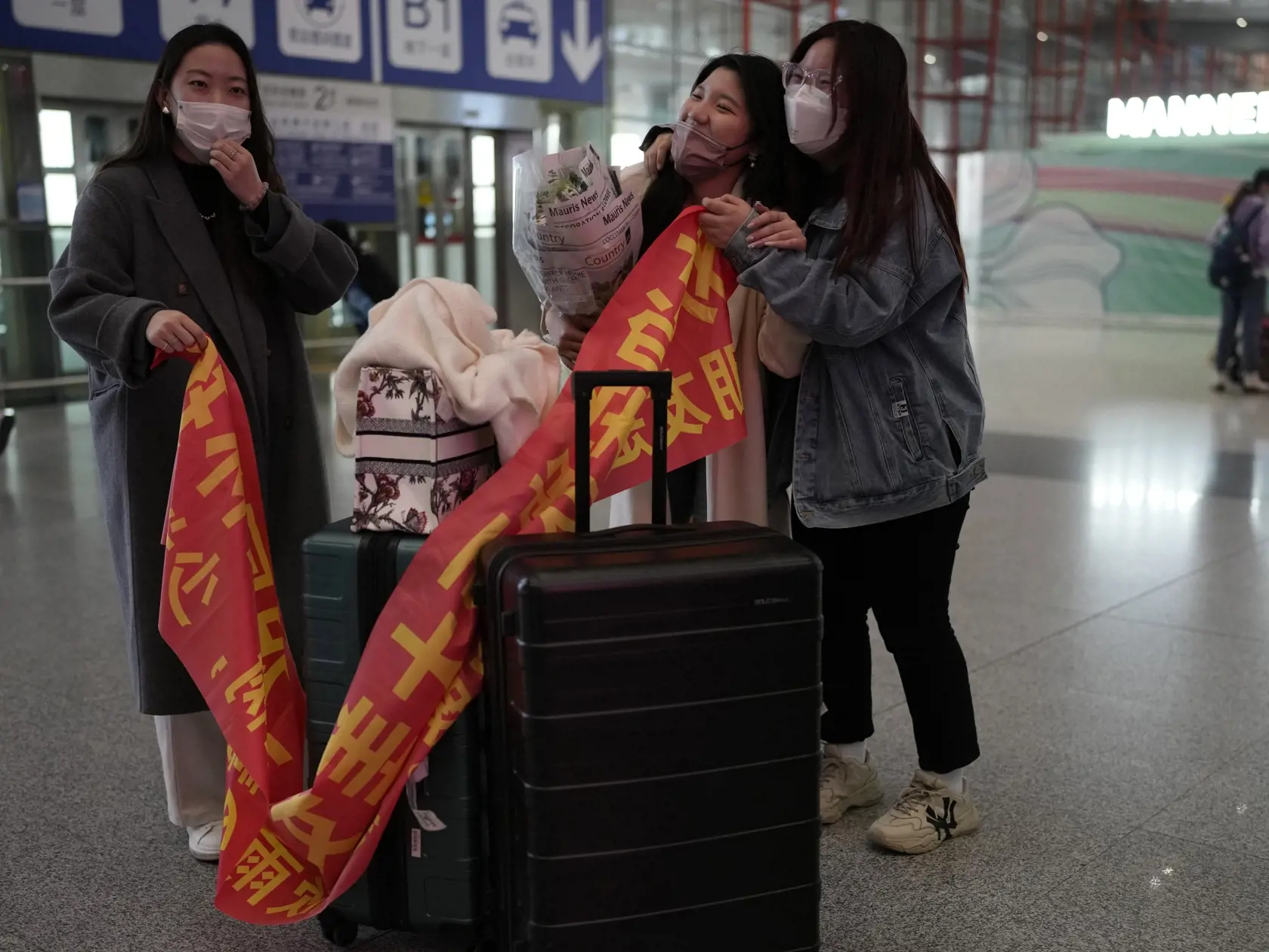 KK37 Peking - Číňanky sa vítajú s kamarátkou na medzinárodnom letisku v Pekingu v utorok 14. marca 2023. Čína obnovila vydávanie rôznych druhov víz pre cudzincov, ktorých udeľovanie bolo pozastavené z dôvodu pandémie ochorenia COVID-19. 
Chinese women unfurl a banner to welcome their friend back at the Beijing Capital International Airport in Beijing, Tuesday, March 14, 2023. China will reopen its borders to tourists and resume issuing all visas Wednesday after a three-year h