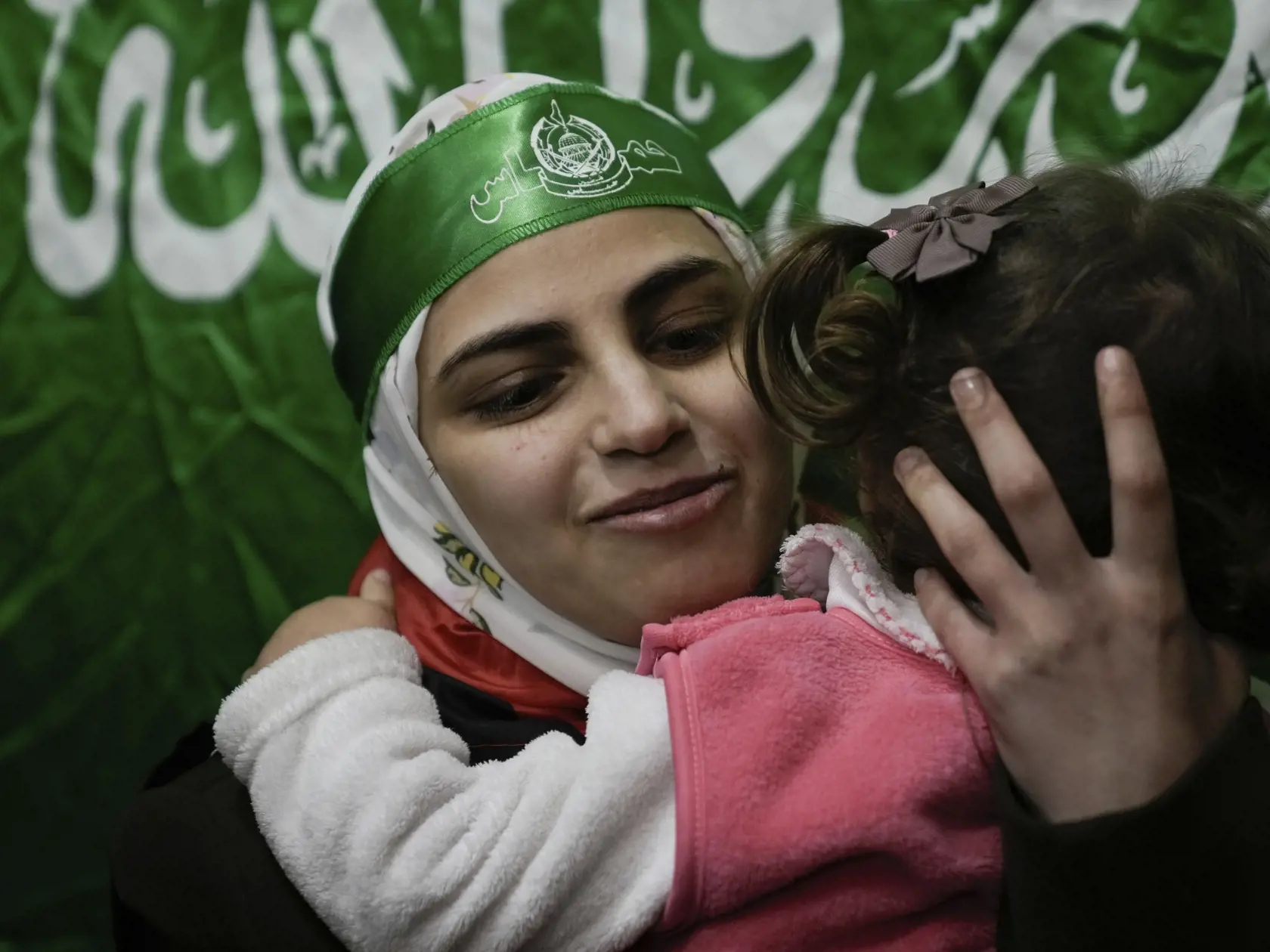Na snímke bývalá palestínska väzenkyňa, ktorá má hlave čelenku Hamasu, sa víta s priateľmi a rodinnými príslušníkmi po jej prepustení v palestínskom utečeneckom tábore v Nábuse na Západnom brehu Jordánu 24. novembra 2023.  Hamas v piatok počas prvého dňa prímeria prepustil prvých 24 z približne 240 rukojemníkov, ktorých zadržiava v Pásme Gazy od útoku na Izrael.