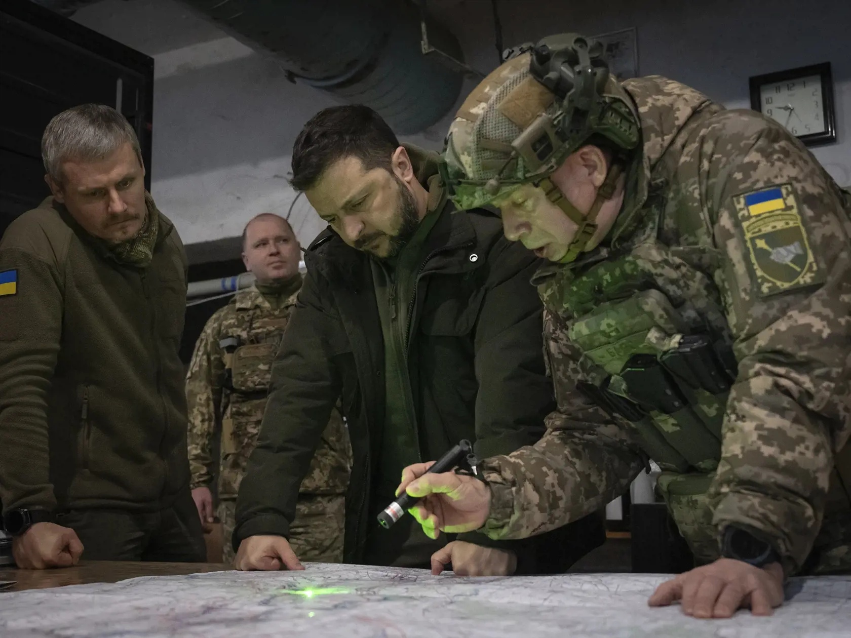 Ukrajinský prezident Volodymyr Zelenskyj (druhý vpravo), veliteľ ukrajinských pozemných síl Oleksandr Syrskij (vpravo) a zástupca vedúceho prezidentskej kancelárie Roman Mašovec (vľavo) sa pozerajú na mapu počas návštevy veliteľského stanovišťa v blízkosti frontu v Charkovskej oblasti na východe Ukrajiny vo štvrtok 30. novembra 2023.