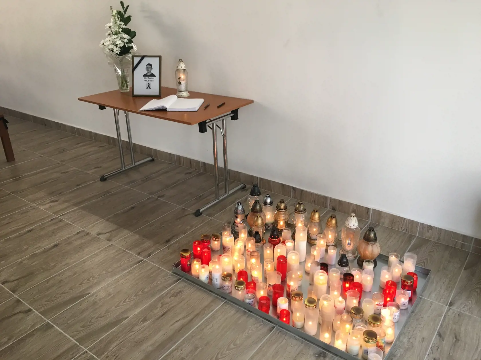 V dome smútku je kondolenčná kniha a ľudia zapaľujú pri fotografií sviečky. 