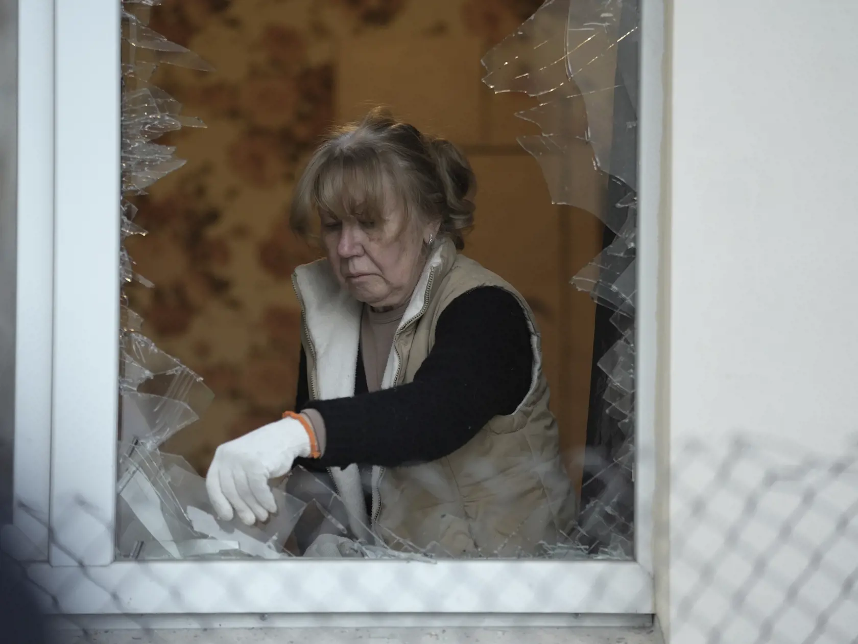 Žena odstrňuje úlomky skla na rozbitom okne po "masívnom útoku" ruských dronov na viacposchodovú obytnú budovu na ukrajinské hlavné mesto Kyjev v utorok 30. mája 2023.