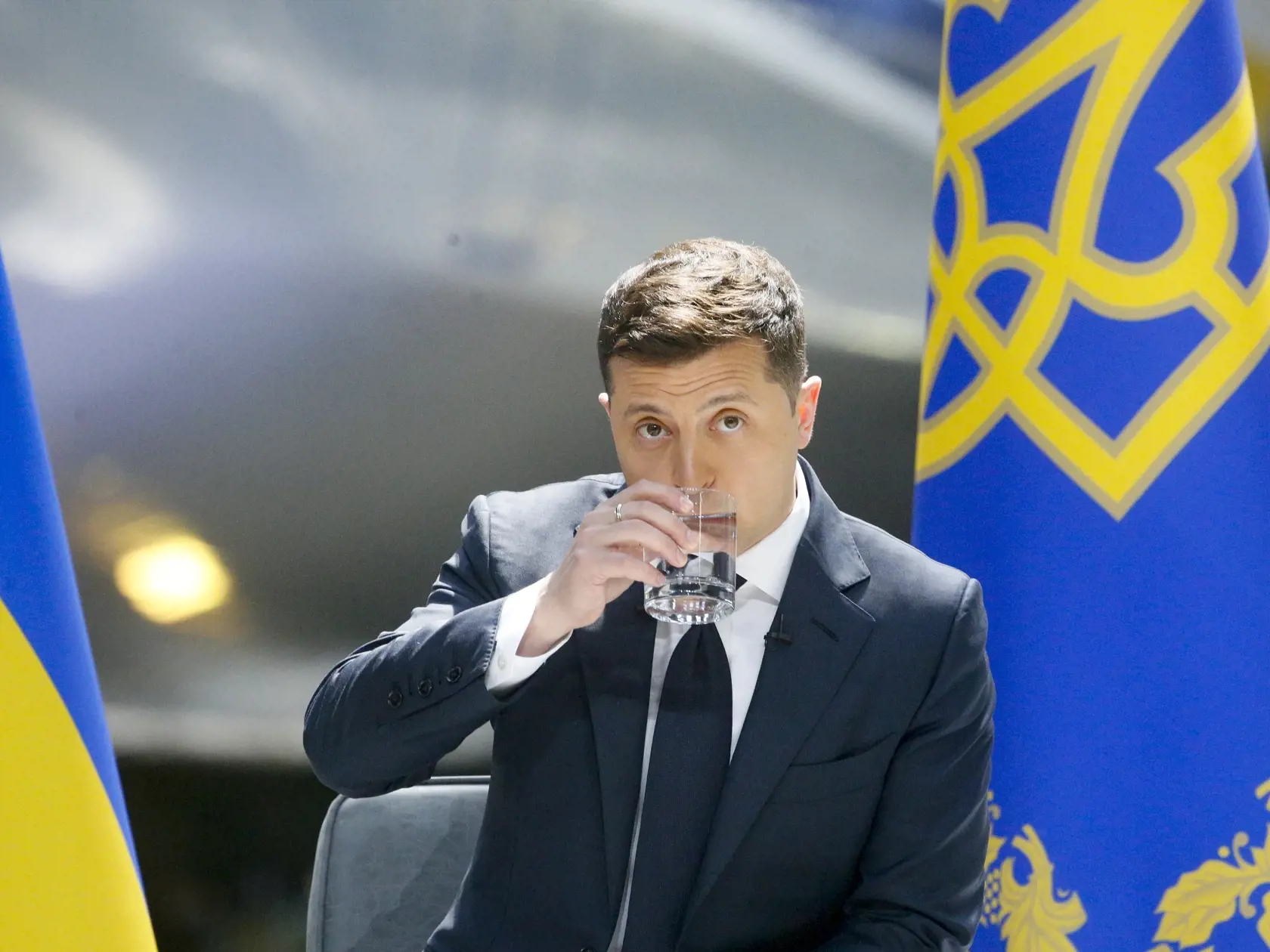Ukrajinský prezident Volodymyr Zelenskyj pije vodu počas výročnej  tlačovej konferencie v závode na výrobu lietadiel Antonov v Kyjeve.