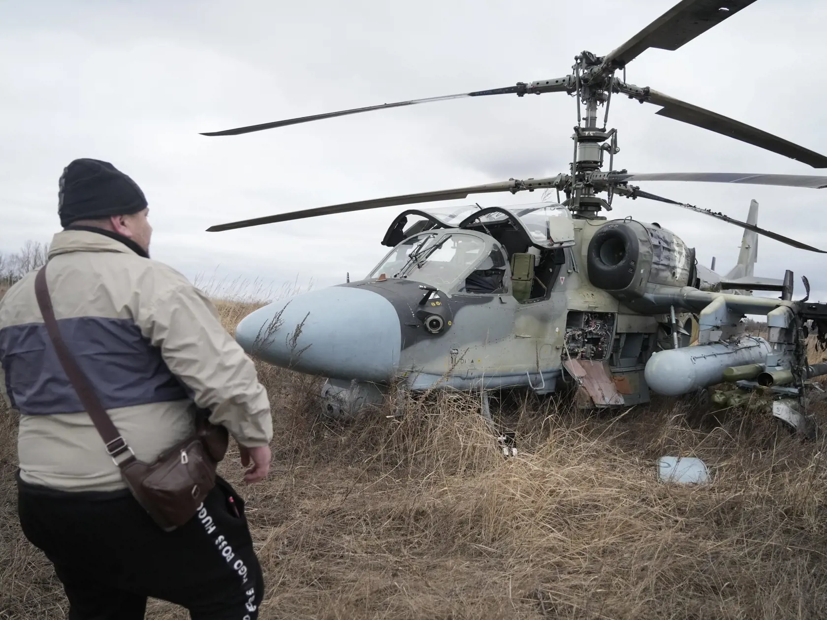 Muž stojí na poli pred ruským bojovým vrtuľníkom Ka-52 po vynútenom pristátí neďaleko Kyjeva.