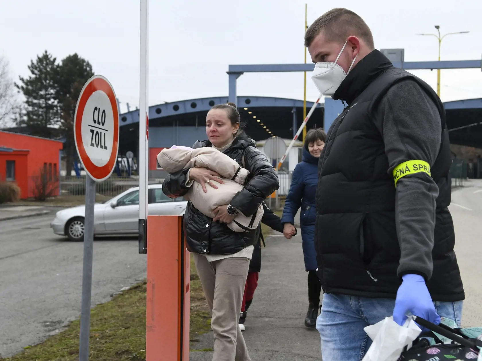 Utečenci z Ukrajiny prechádzajú cez hraničný priechod vo Vyšnom Nemeckom, vpravo im pomáha príslušník Finančnej správy SR. Vyšné Nemecké, 25. februára 2022. FOTO TASR - Milan Kapusta