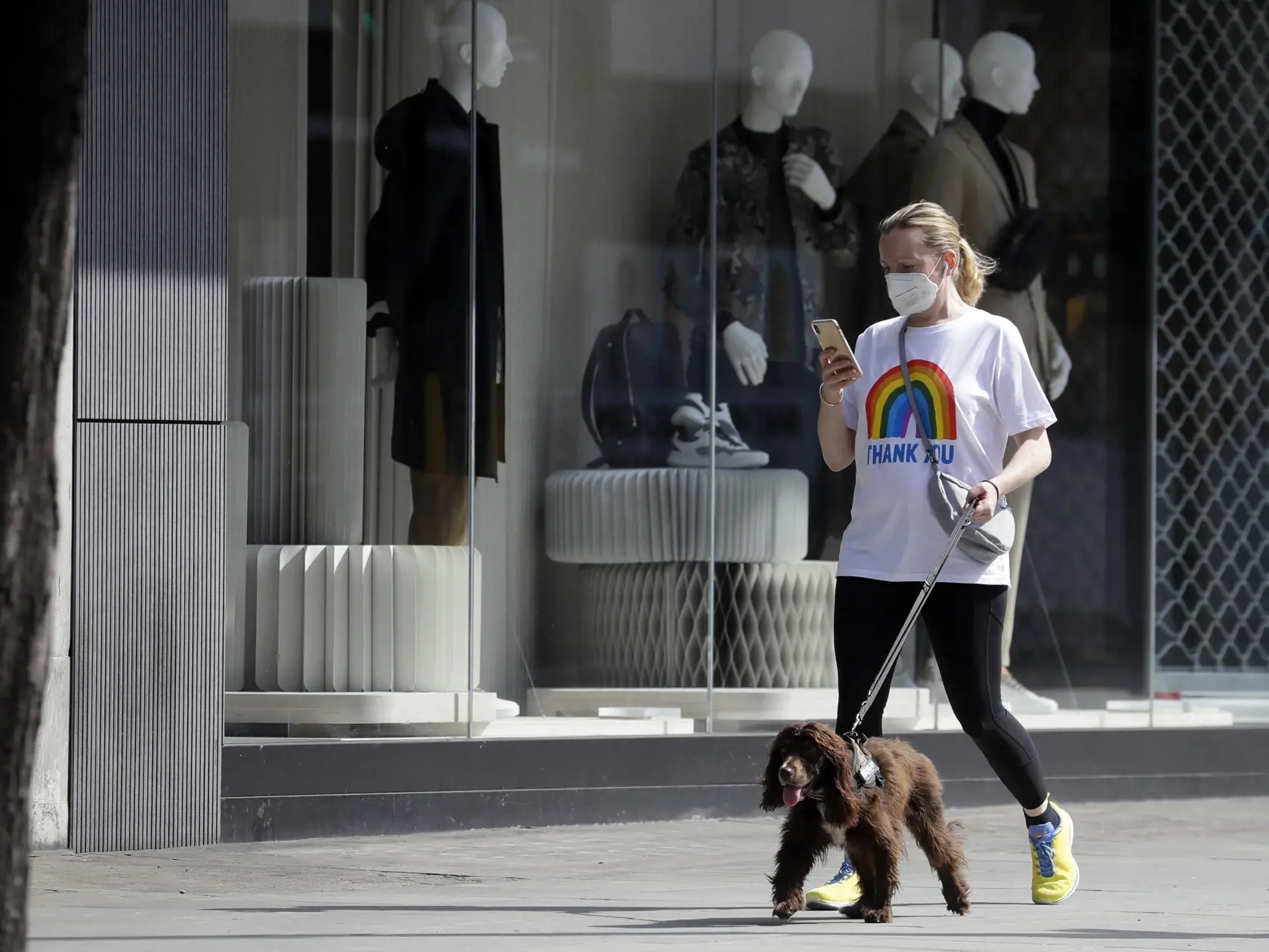Žena s ochranou maskou na zabránenie šíreniu nového koronavírusu prechádza so psom okolo zatvoreného obchodu na ulici Oxford Street v Londýne.
