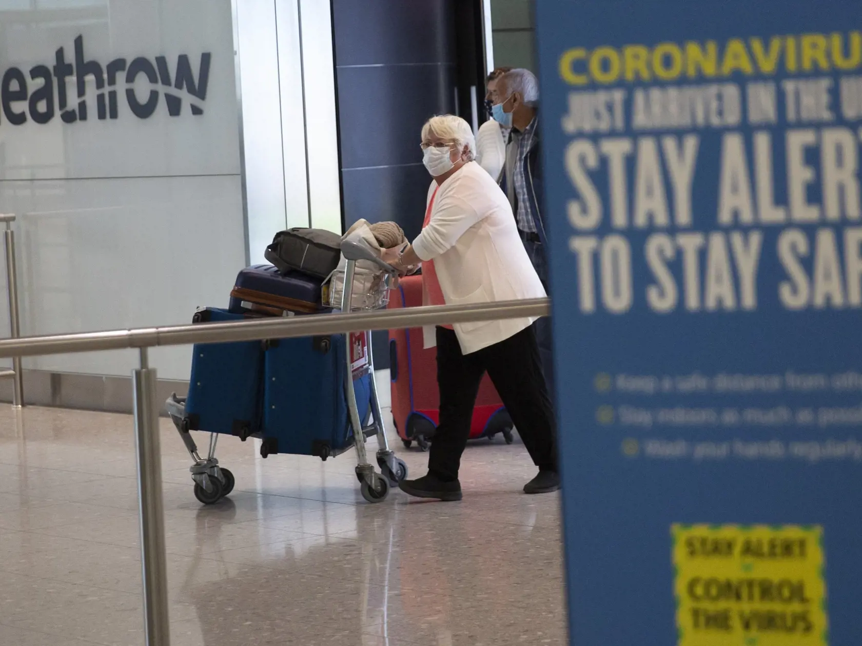 Pasažieri s ochrannými rúškami na zabránenie šírenia nového koronavírusu kráčajú po ich prílete na letisko Heathrow v Londýne.