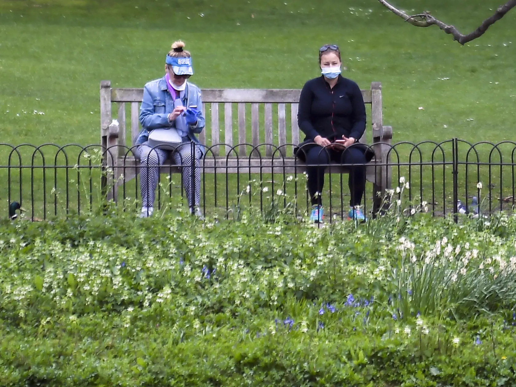 Ľudia sedia na lavičke s ochrannými rúškami na zabránenie šíreniu nového koronavírusu a so sociálnym odstupom v parku St James's Park  v Londýne.