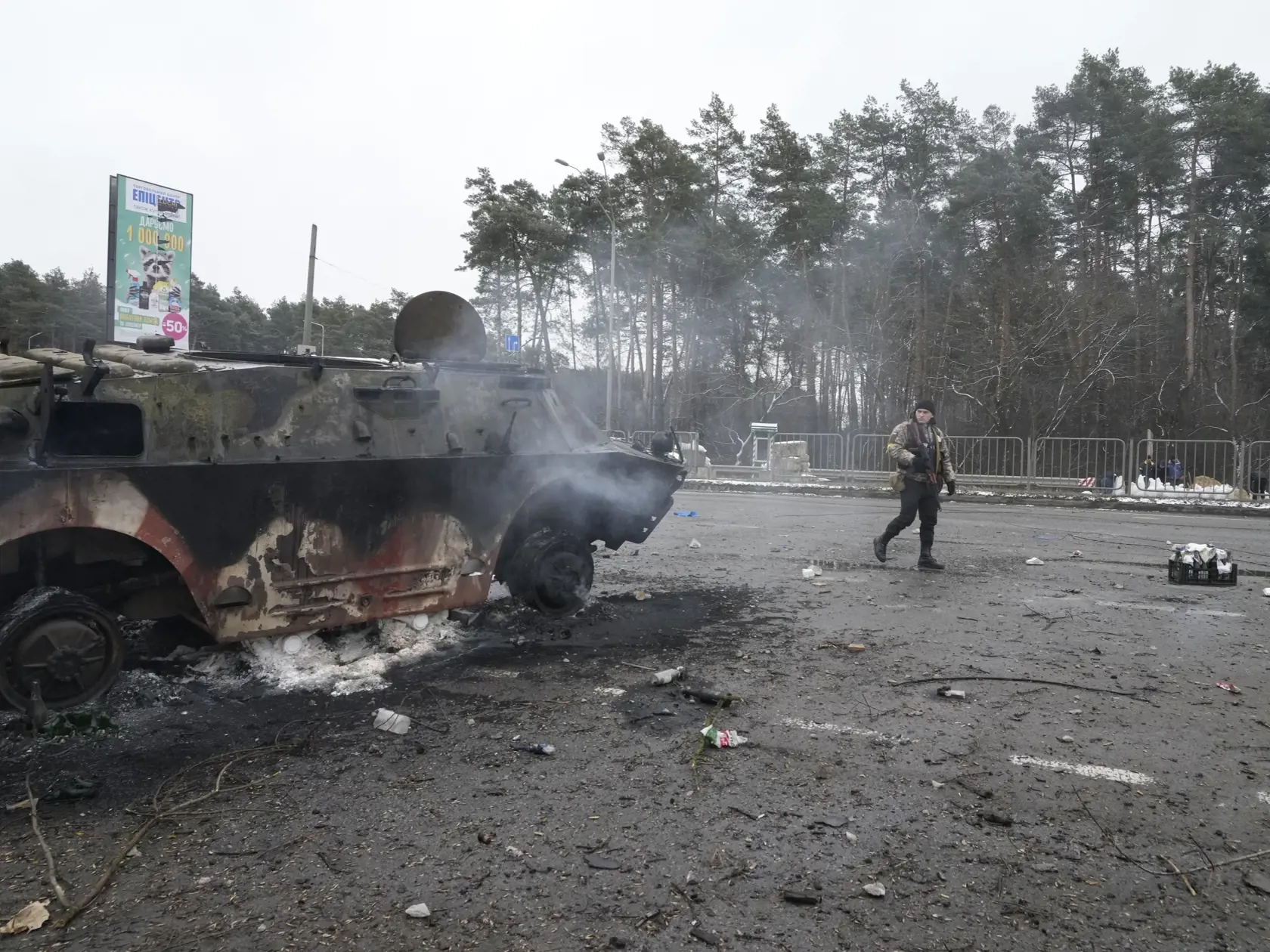 KK38 Brovary - Dobrovoľník jednotiek územnej obrany ukrajinskej armády kráča okolo zničeného armádneho vozidla v ukrajinskom meste Brovary neďaleko Kyjeva v utorok 1. marca 2022.