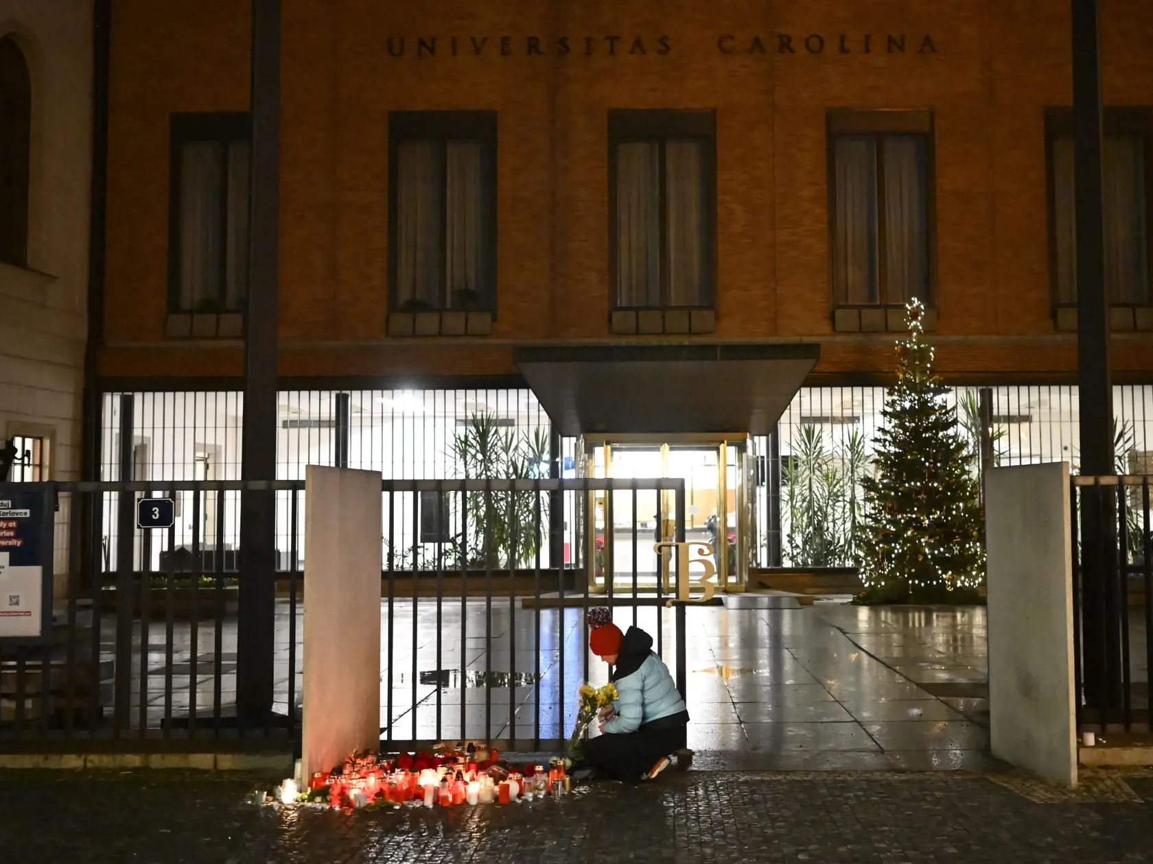 Žena zapaľuje sviečku pred budovou Filozofickej fakulty Univerzity Karlovej (FF UK) pre obete masovej streľby v centre Prahy 22. decembra 2023.