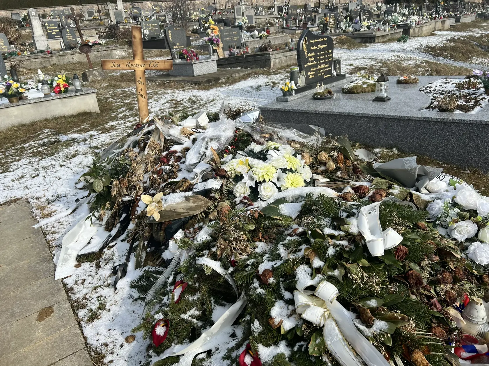 Namiesto pomníka tu dočasne stojí len jednoduchý drevený kríž a hrob pôsobí ako keby sa oň nik nestaral - ležia na ňom staré kvety ešte od pohrebu.
