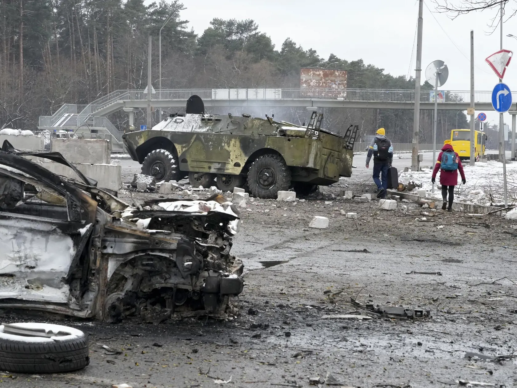 KK37 Brovary - Ľudia kráčajú okolo zničených aút a armádneho vozidla v ukrajinskom meste Brovary neďaleko Kyjeva v utorok 1. marca 2022.